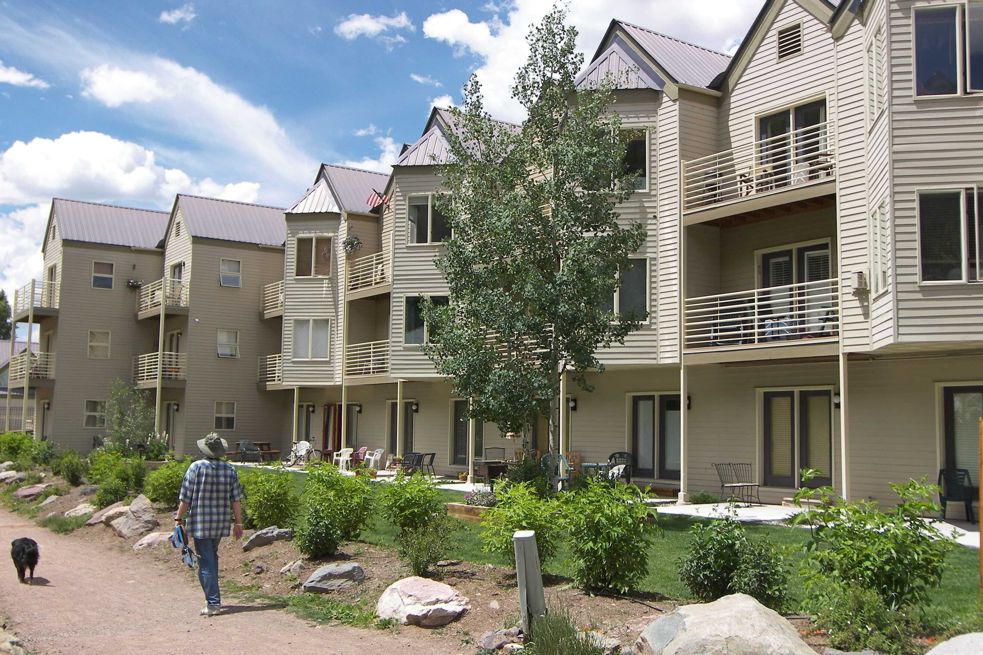 A multi-story building with balconies, a patio area with outdoor seating, and a well-maintained garden.