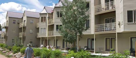 A multi-story building with balconies, a patio area with outdoor seating, and a well-maintained garden.