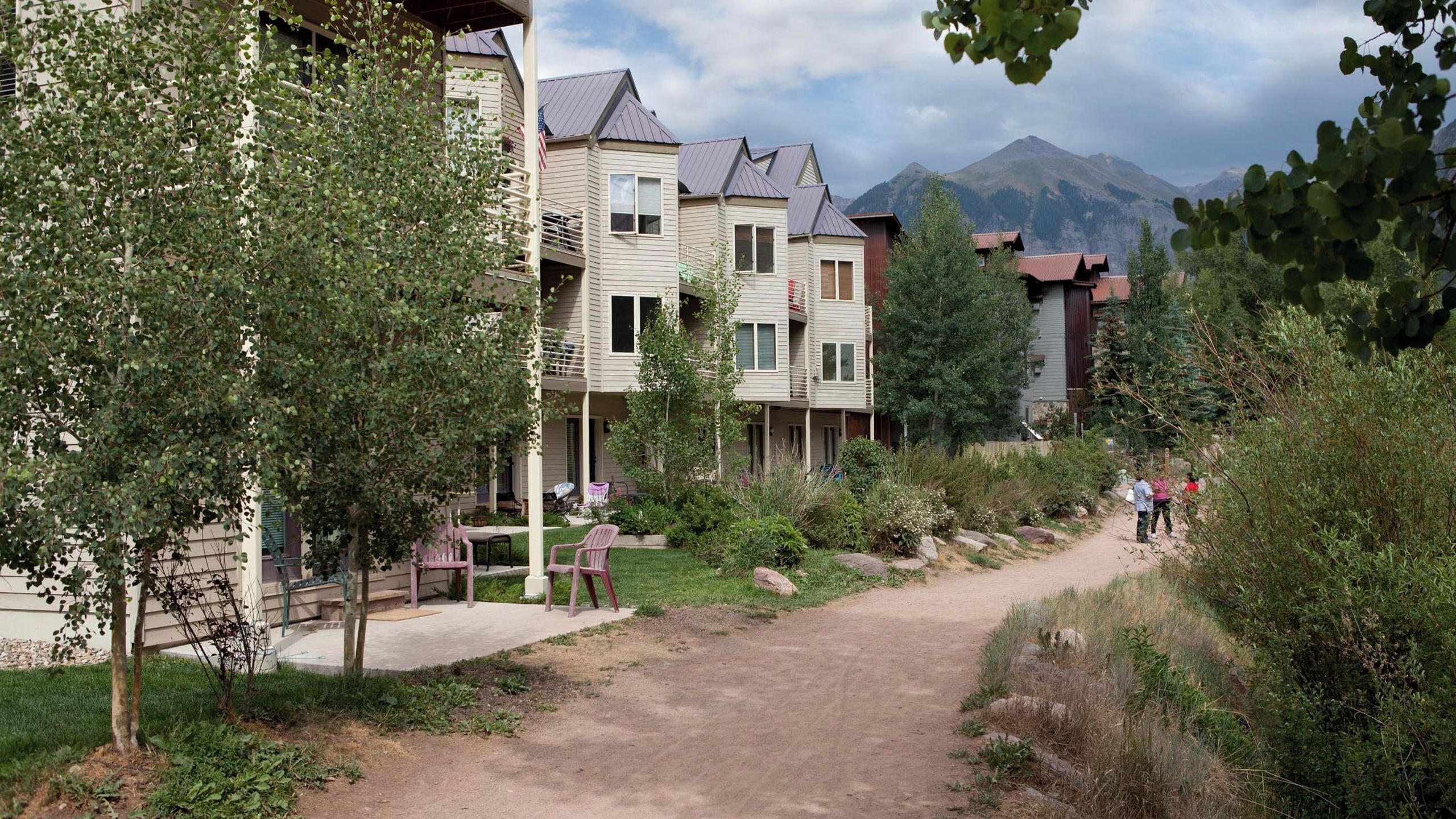 A residential area with multi-story buildings, a dirt path, and a mountain in the background.