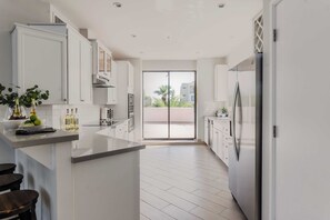 A modern kitchen with white cabinetry, a central island, and a large sliding glass door leading to a balcony. - Ivory II By Avantstay Gorgeous Spacious Home w/ Views Close To Old Town (Scottsdale)
