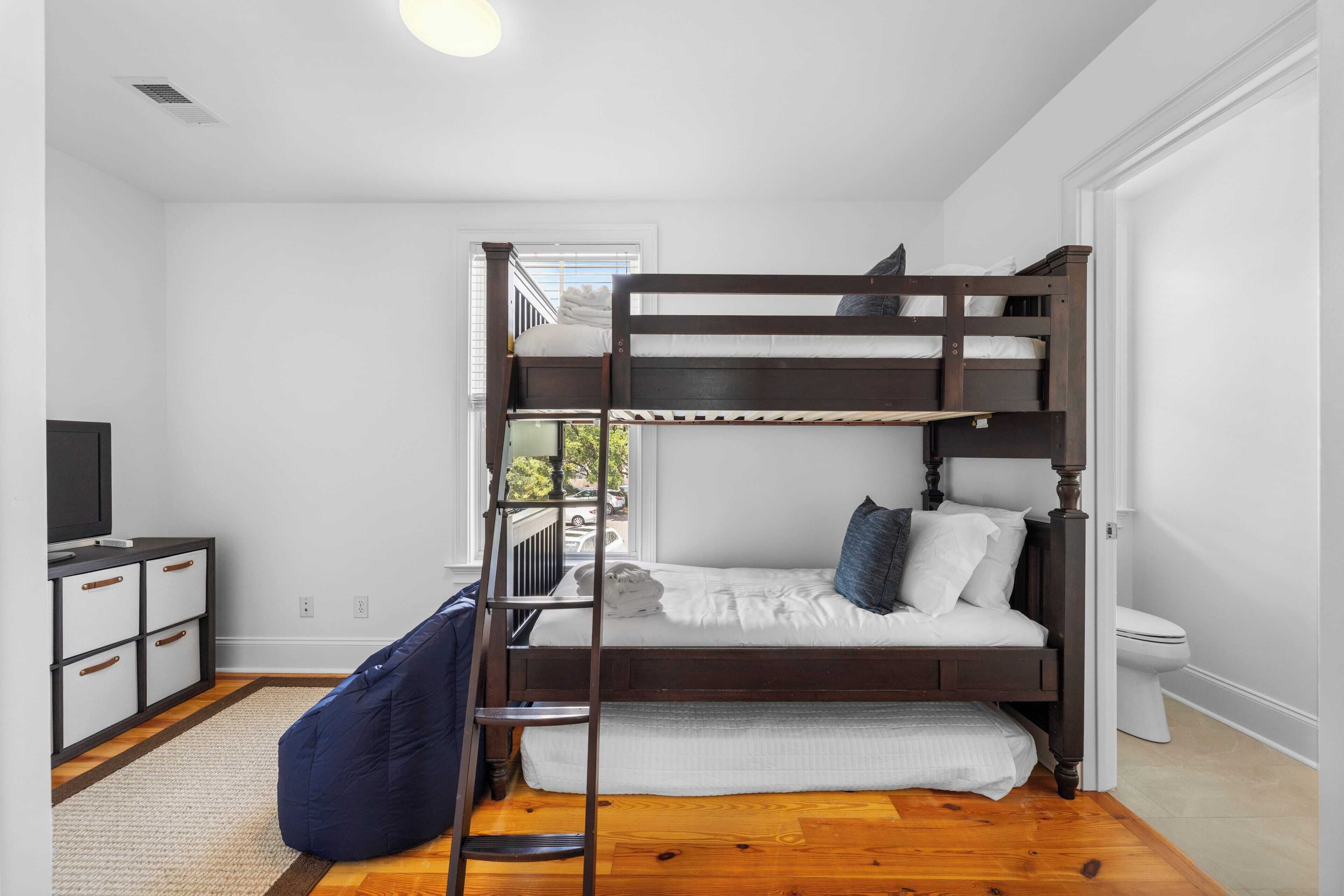A bunk bed room with a TV, dresser, and a view of the outdoors.