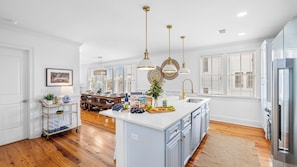A modern kitchen with a central island, pendant lights, and a dining area with a wooden table. - 1 Block to Beach, Newly Renovated 6bdr w/ Rooftop Views Sand Dune by Avantstay (Isle of Palms)