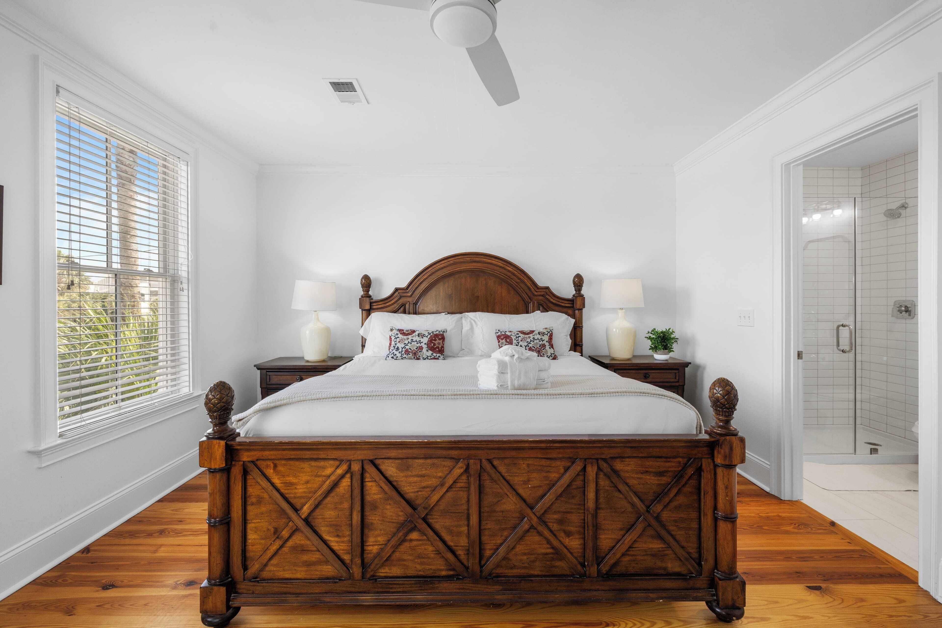 A bedroom with a wooden bed, white walls, and a window with blinds.