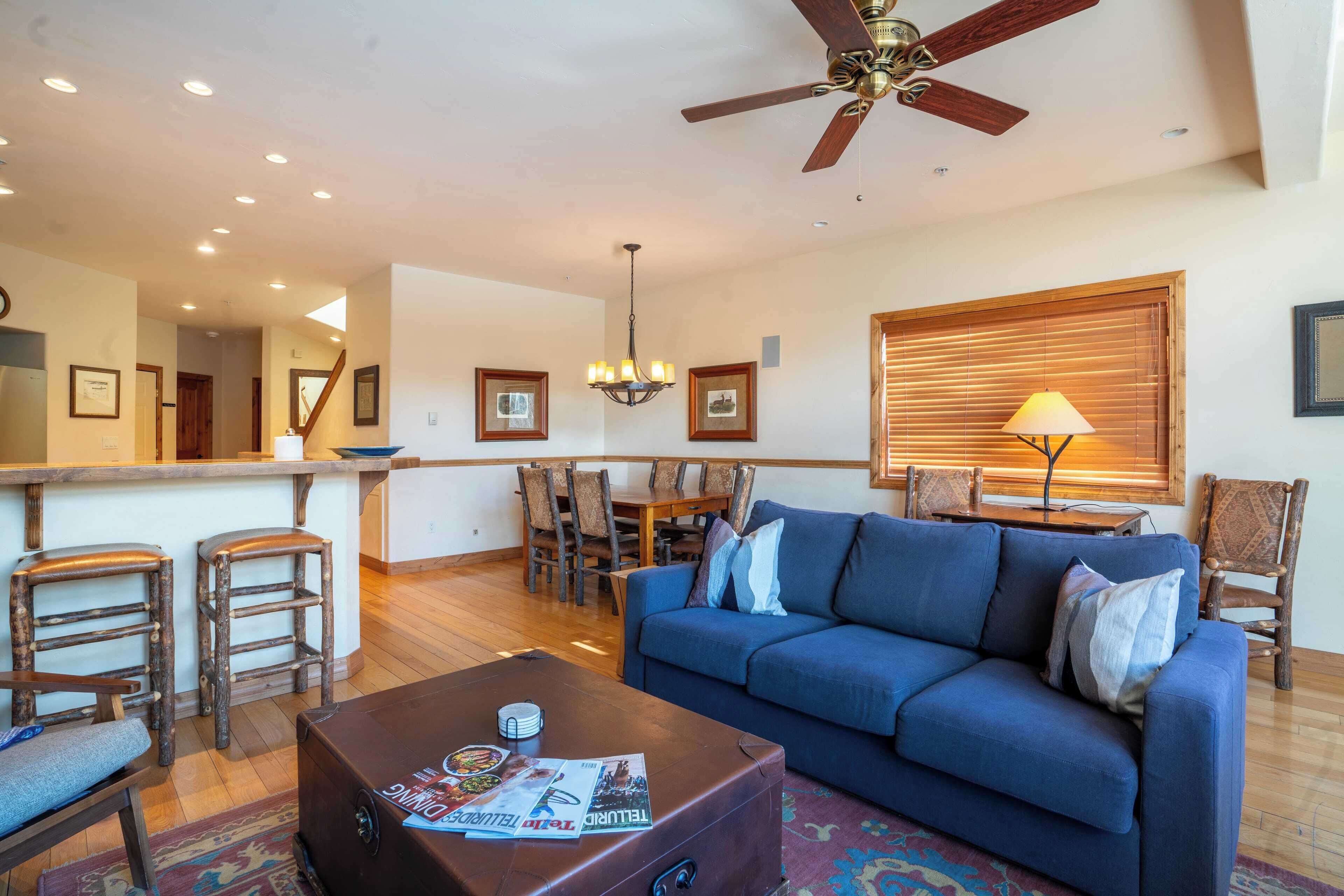 A living room with a blue sofa, wooden chairs, a coffee table, and a ceiling fan.