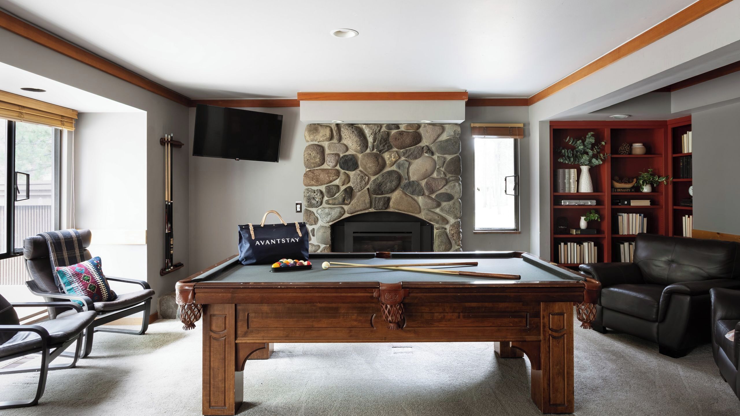 A pool table with a stone fireplace, a bookshelf, and a leather chair.