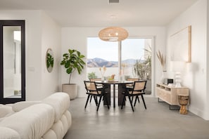 A modern dining area with a round table, black chairs, and a large window offering a mountain view. - Aria by Avantstay Spectacular & Secluded Desert Oasis w/ Pool (Yucca Valley)