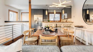 A modern kitchen with a dining area, featuring a wooden table, chairs, and a contemporary light fixture.
