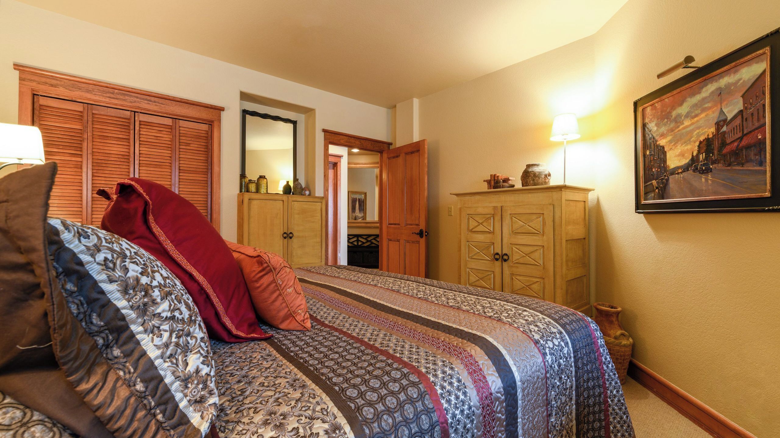 Une chambre à coucher avec un lit, une armoire, un miroir et un tableau accroché au mur.