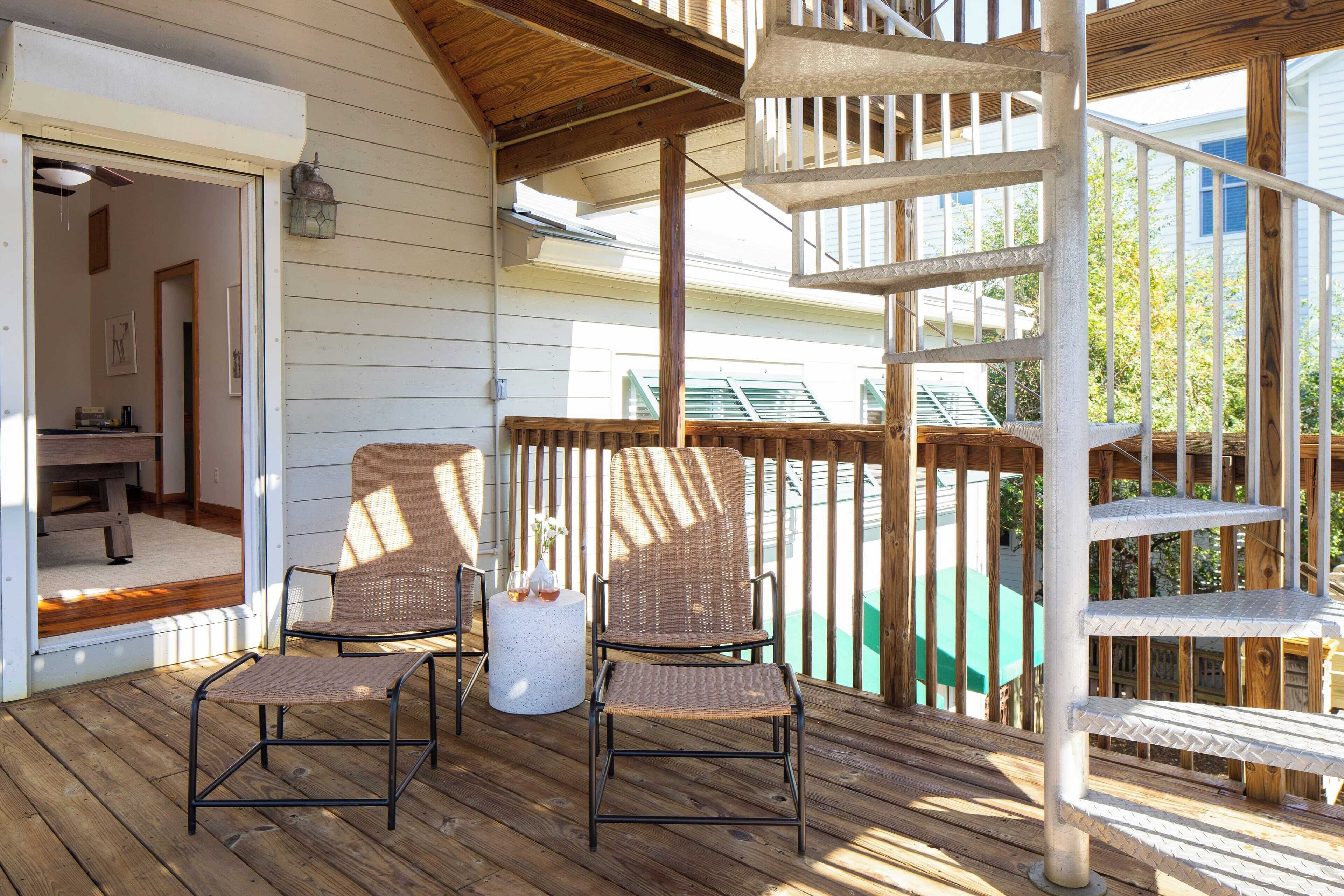 A wooden deck with two wicker chairs, a small round table, and a spiral staircase.