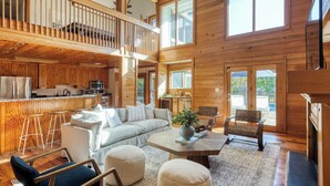 A spacious living area with a high ceiling, wooden walls, a kitchen with modern appliances, and a cozy seating arrangement. - Raven by Avantstay Entertainers Dream w/ Pool, Hot Tub, Game Room! 9 Brs! (Sullivan's Island)