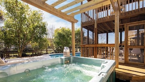 A wooden deck with a hot tub, surrounded by trees and a pool. - Raven by Avantstay Entertainers Dream w/ Pool, Hot Tub, Game Room! 9 Brs! (Sullivan's Island)
