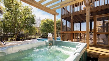 A wooden deck with a hot tub, surrounded by trees and a pool.