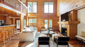 A spacious cabin interior with a kitchen, dining area, and living room, featuring wooden walls and a high ceiling. - Raven by Avantstay Entertainers Dream w/ Pool, Hot Tub, Game Room! 9 Brs! (Sullivan's Island)