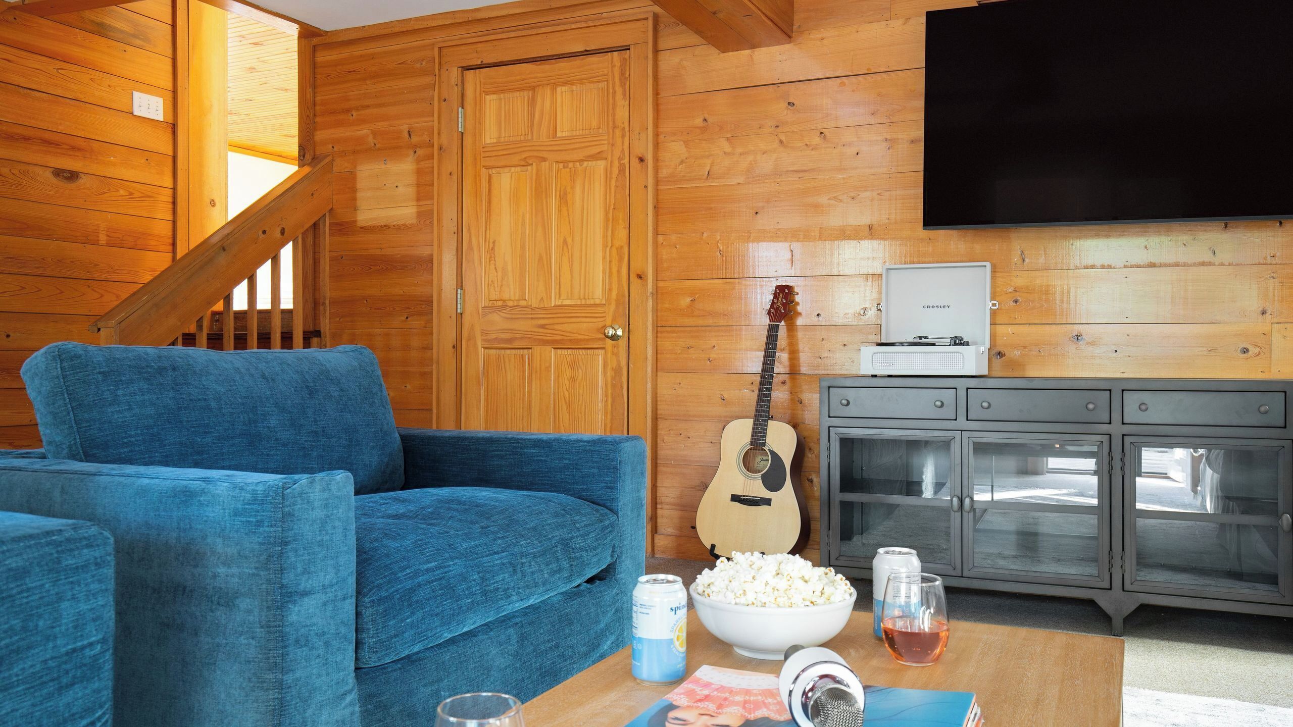 Una sala de estar acogedora con un sofá azul, una guitarra, un televisor y un aparador con puertas de cristal.