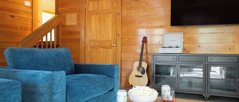 Una sala de estar acogedora con un sofá azul, una guitarra, un televisor y un aparador con puertas de cristal.