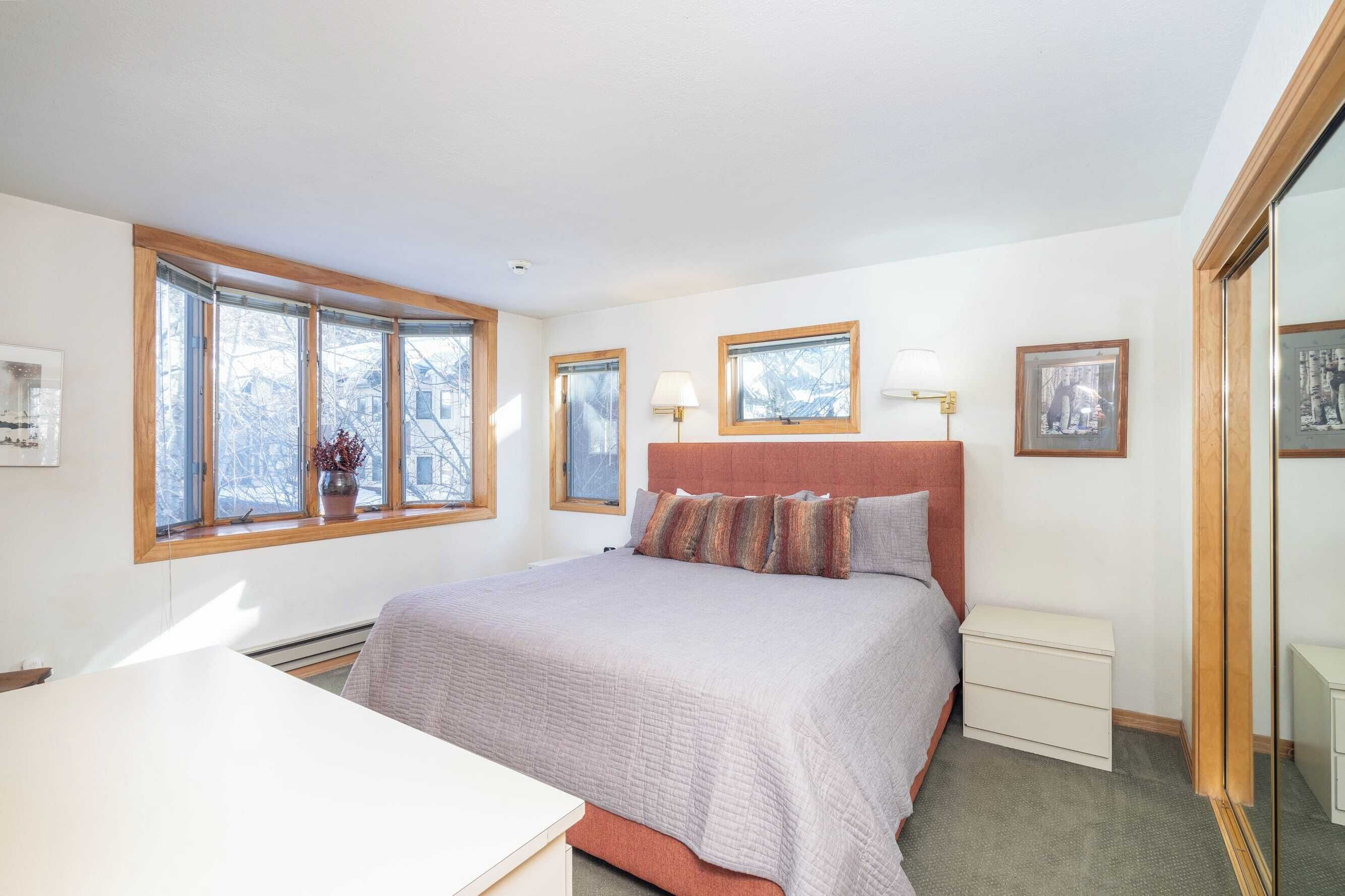 A bedroom with a large bed, two bedside tables, a window with a view, and a mirror.