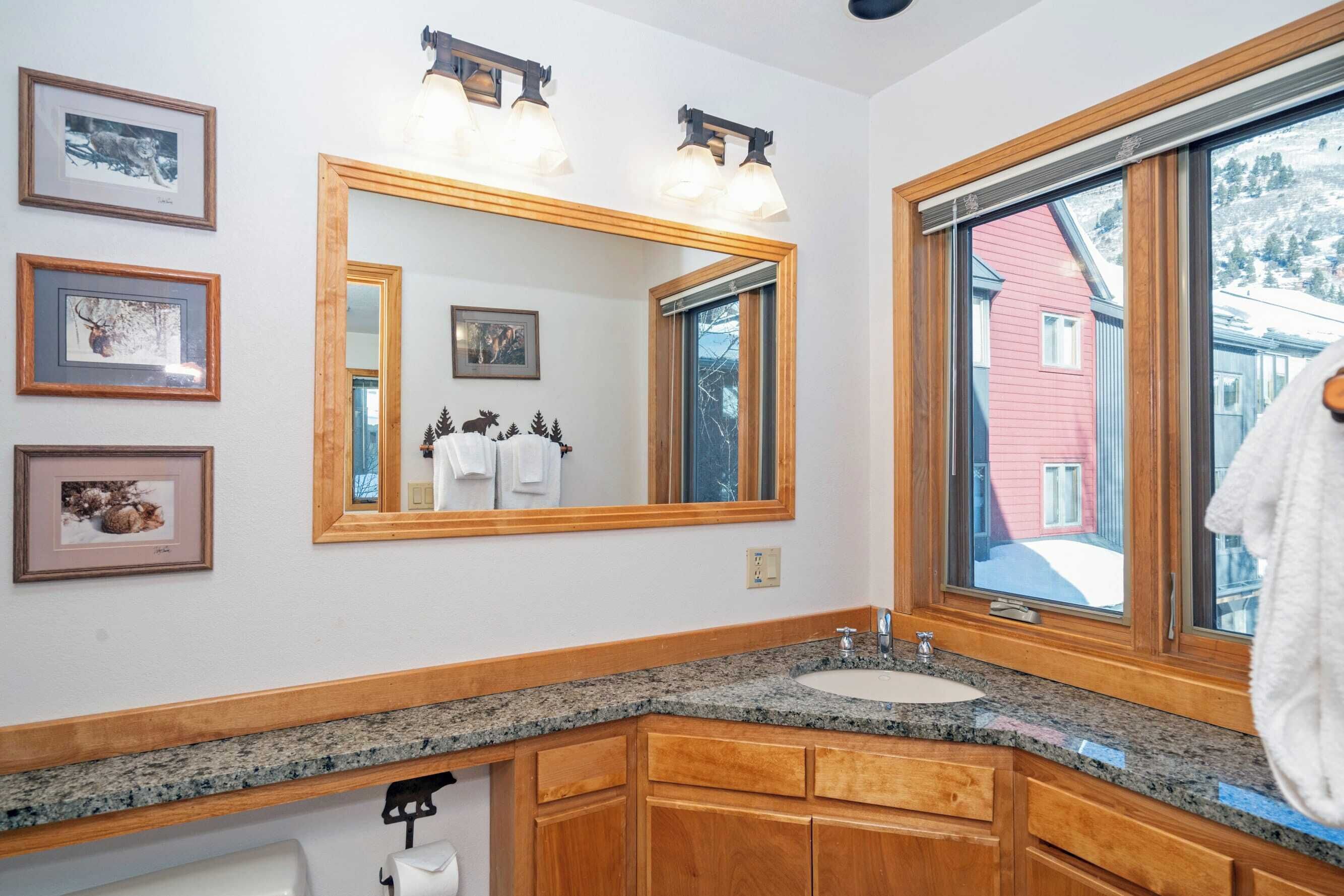 A bathroom with a large mirror, wooden cabinets, a granite countertop, and framed pictures on the wall.