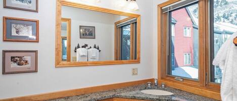 A bathroom with a large mirror, wooden cabinets, a granite countertop, and framed pictures on the wall.