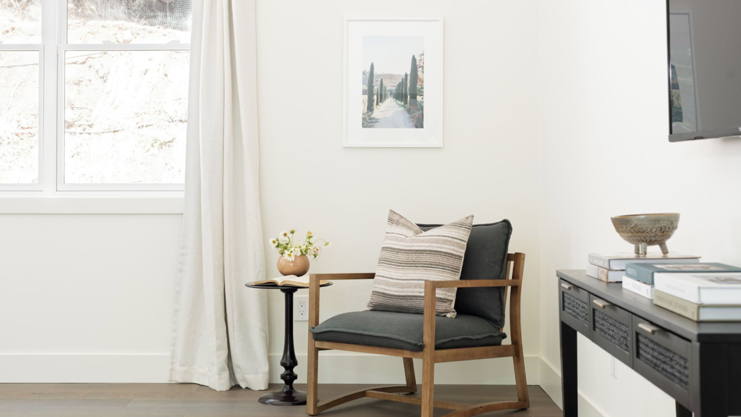 A room with a wooden chair, a small table with a vase, and a framed picture on the wall.
