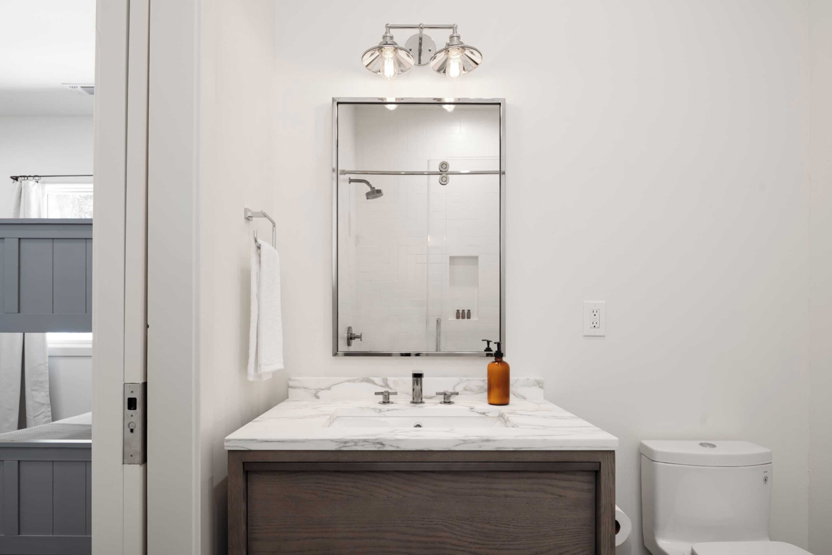A modern bathroom with a glass shower enclosure, a marble sink, and a wooden vanity.