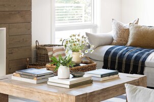 Un salón acogedor con una mesita de madera, libros, una planta en maceta y una cesta de mimbre.