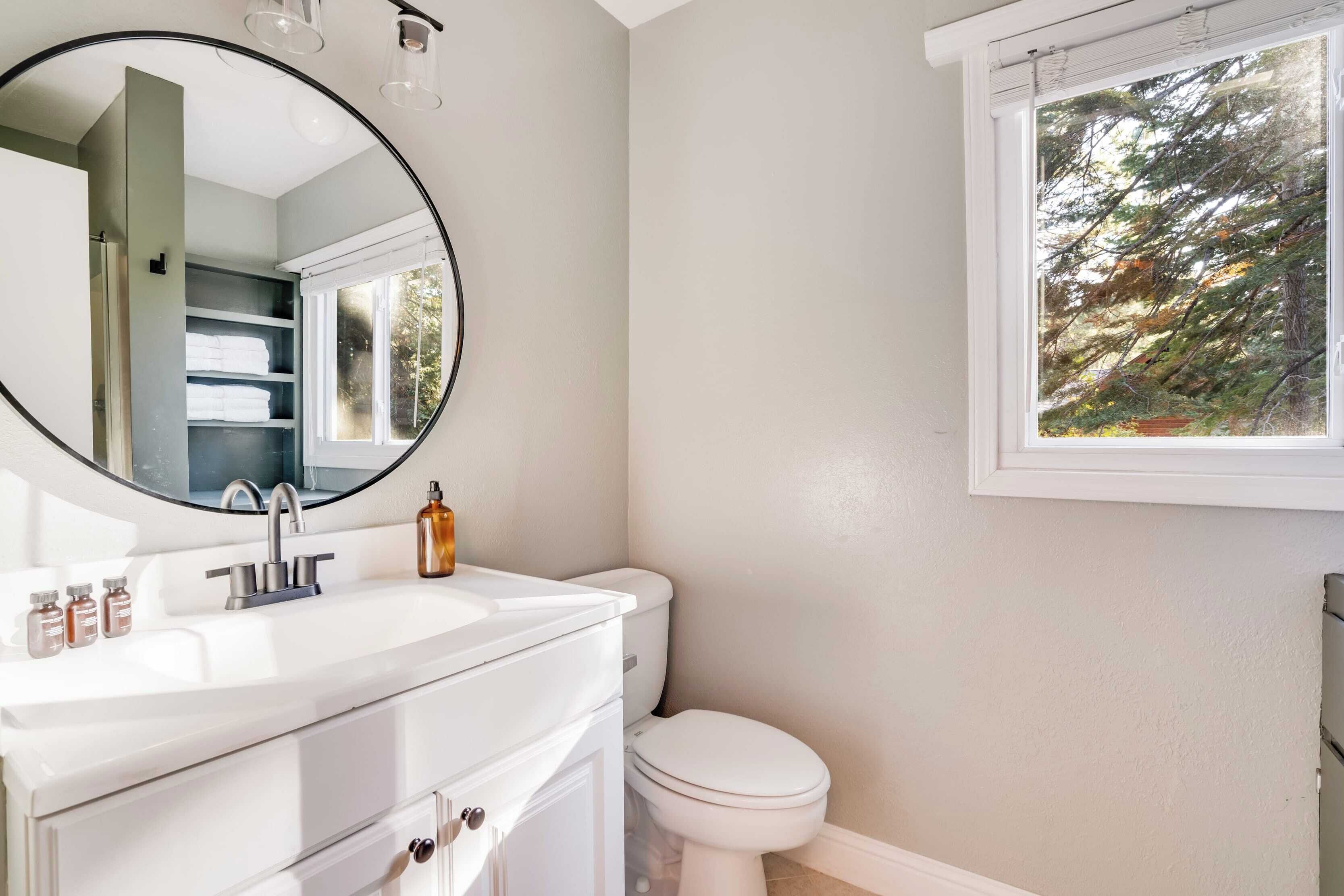 Une salle de bain avec un lavabo blanc, un miroir rond et des toilettes.
