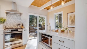 A modern kitchen with a stove, oven, microwave, and a large window overlooking a deck. - Hot Tub, Sauna, Game Room Modern 5bdr Family Cabin Homewood by Avantstay (Homewood)
