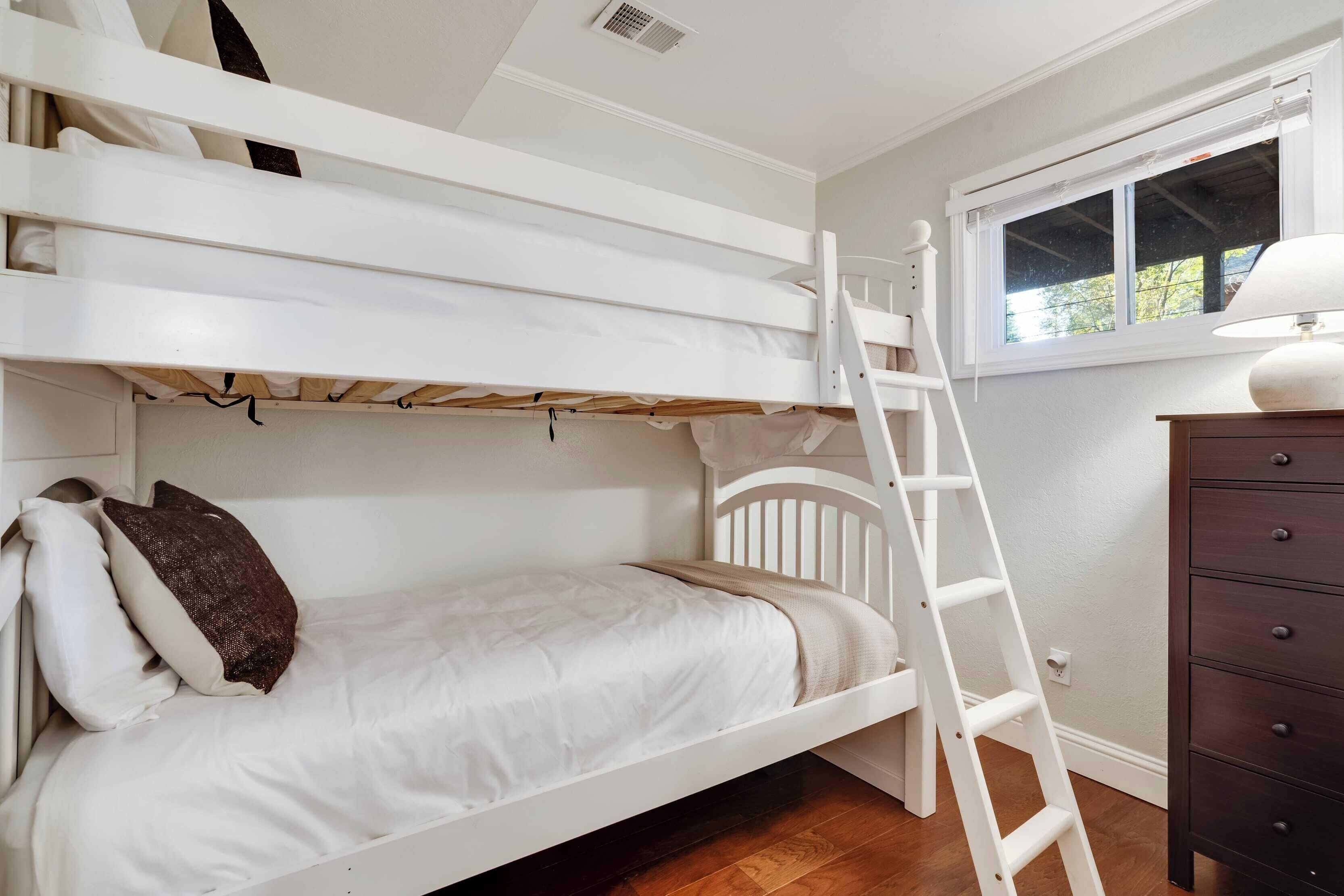 Une chambre avec un lit superposé, une échelle, une commode et une fenêtre.