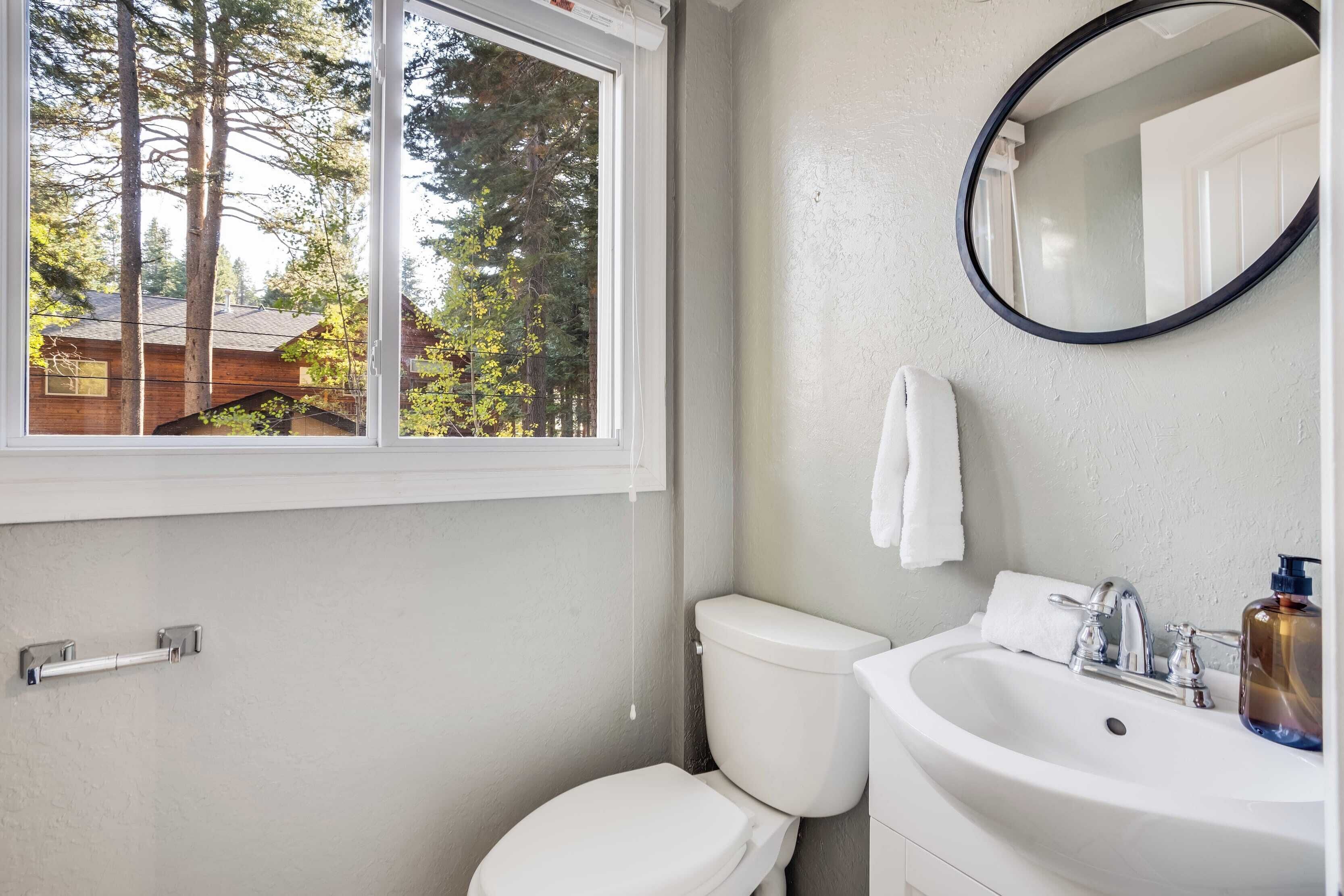 A bathroom with a toilet, sink, and window.