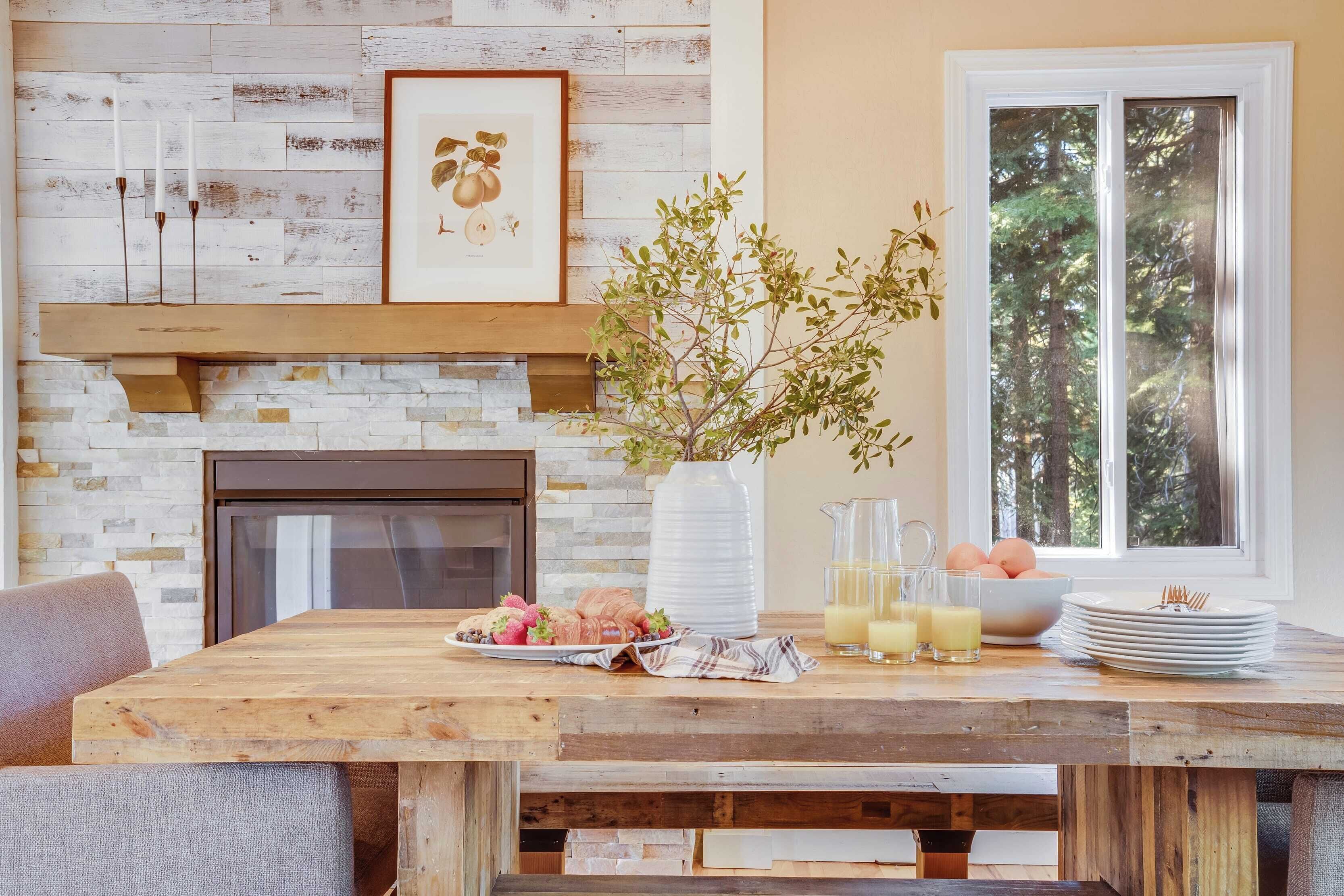 A wooden dining table with a fruit platter, a vase with branches, and a pitcher of juice.