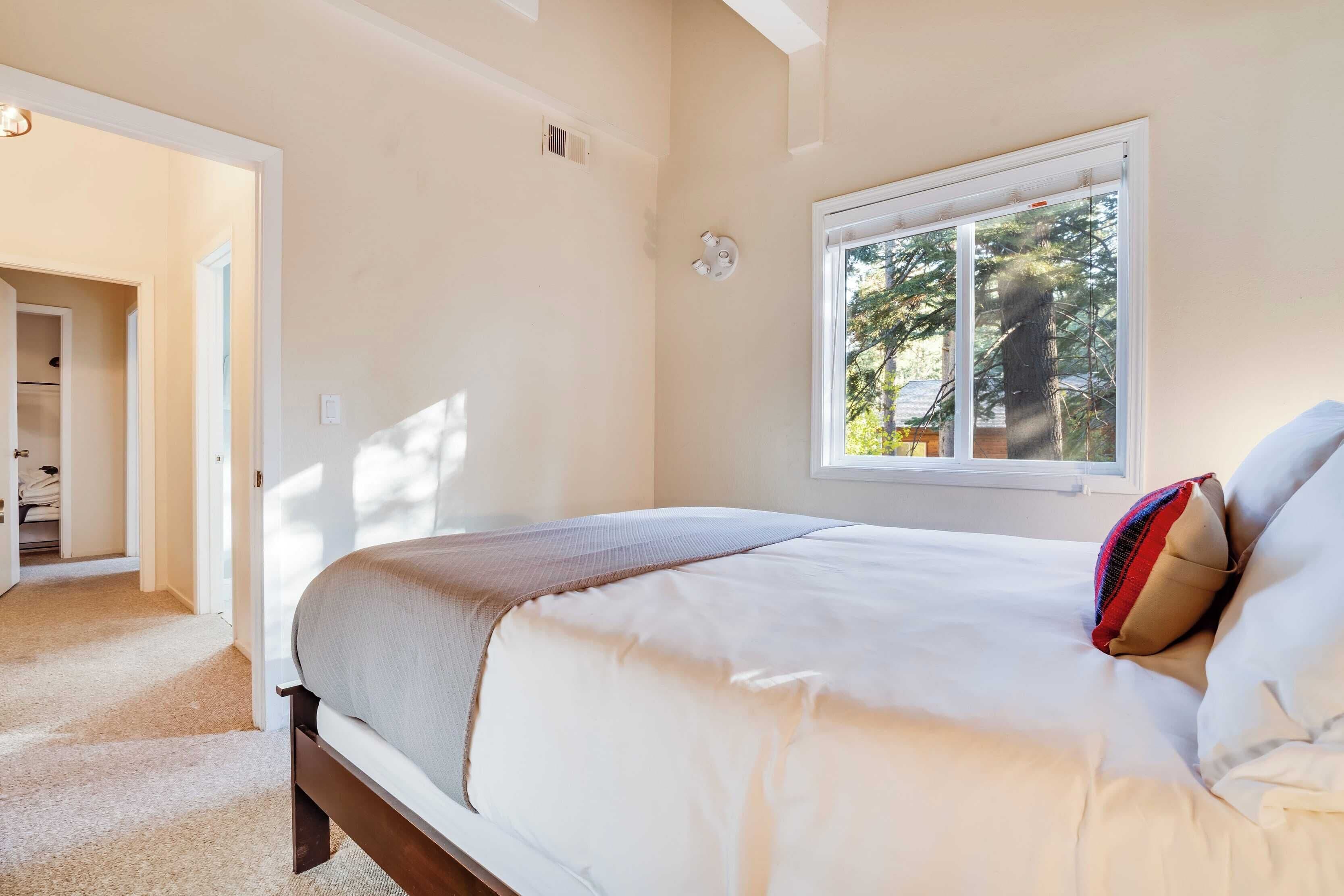 A bedroom with a bed, a window, and a door leading to a hallway.