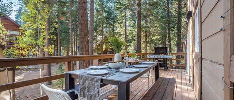 A deck with a table set for dining, surrounded by tall trees.