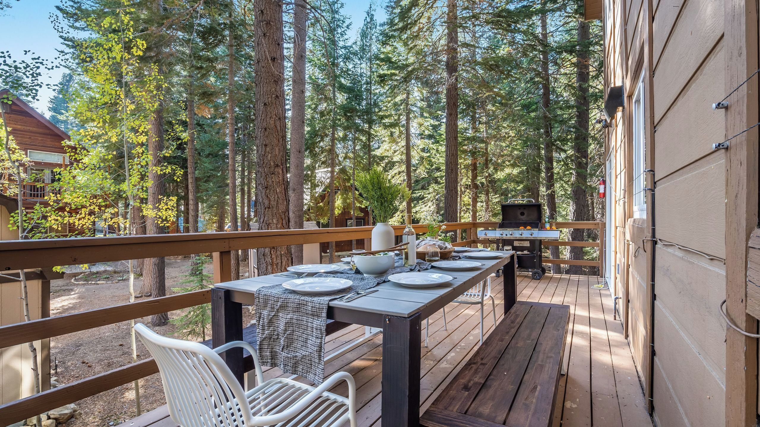 A wooden deck with a table set for dining, surrounded by tall trees.