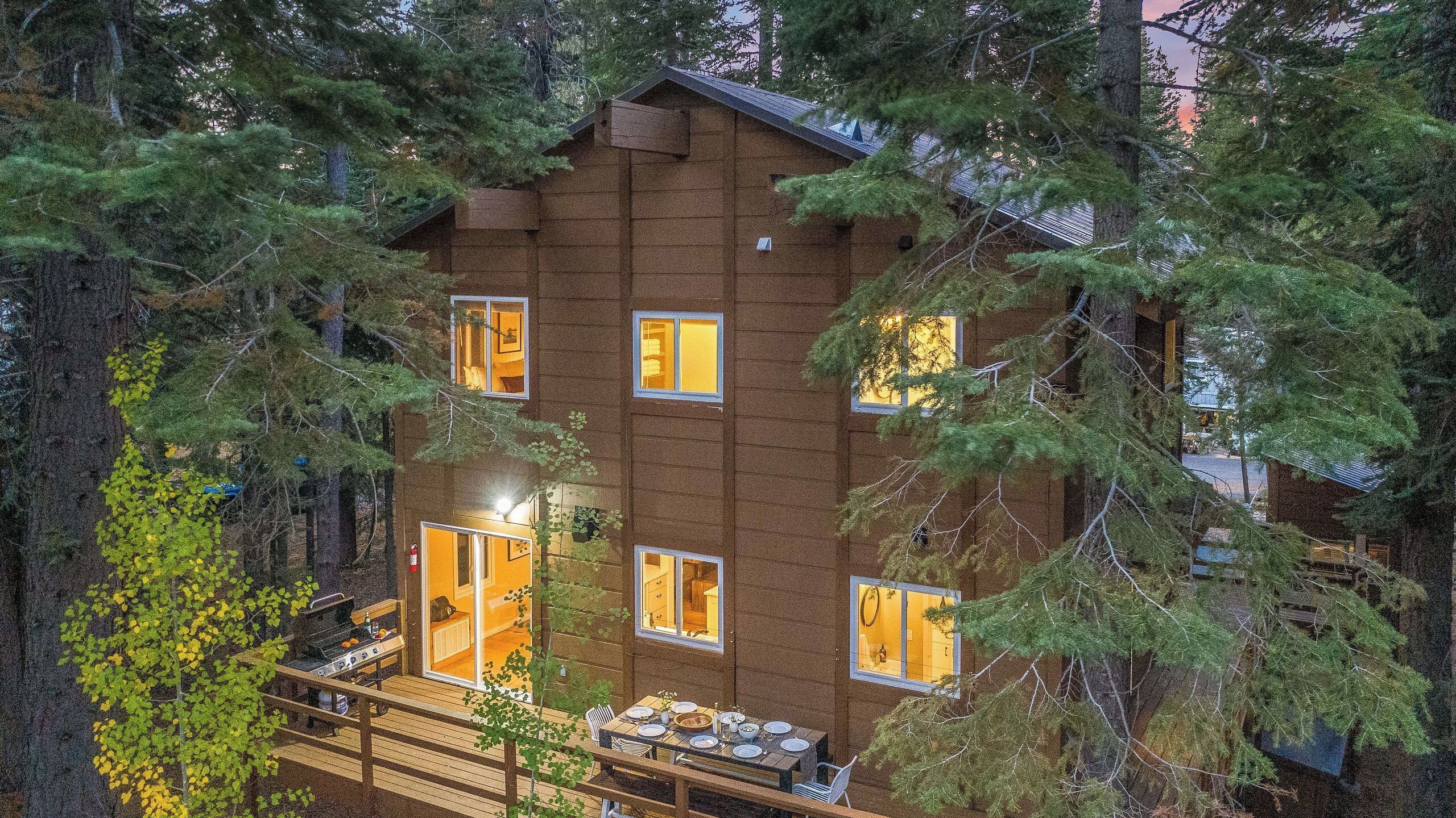 Une cabane dotée de nombreuses fenêtres, d’une terrasse avec des sièges d’extérieur et d’un intérieur visible, comprenant un coin repas.