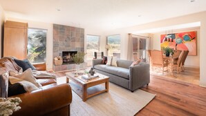 A spacious living room with a fireplace, leather sofas, a dining area with a table and chairs, and large windows offering a view of the outdoors. - Picasso by Avantstay Artist's Mountain Escape w/ Hot Tub & Views (Park City)