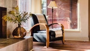 A cozy room with a fireplace, a black leather chair with wooden armrests, a vase with yellow flowers, and a lamp. - Picasso by Avantstay Artist's Mountain Escape w/ Hot Tub & Views (Park City)