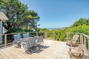 Eine Holzterrasse mit Tisch und Stühlen, umgeben von Grünpflanzen und mit Blick auf eine schöne Aussicht.