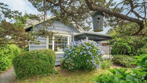 A house with a covered porch, a birdhouse, and a garden with hydrangea bushes. - Beach Pines Bungalow by Avantstay Classic Cottage Steps to the Beach w/ Private Yard (Arch Cape)