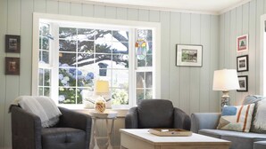 A living room with a large window, two armchairs, a sofa, a small table, and a lamp. - Beach Pines Bungalow by Avantstay Classic Cottage Steps to the Beach w/ Private Yard (Arch Cape)