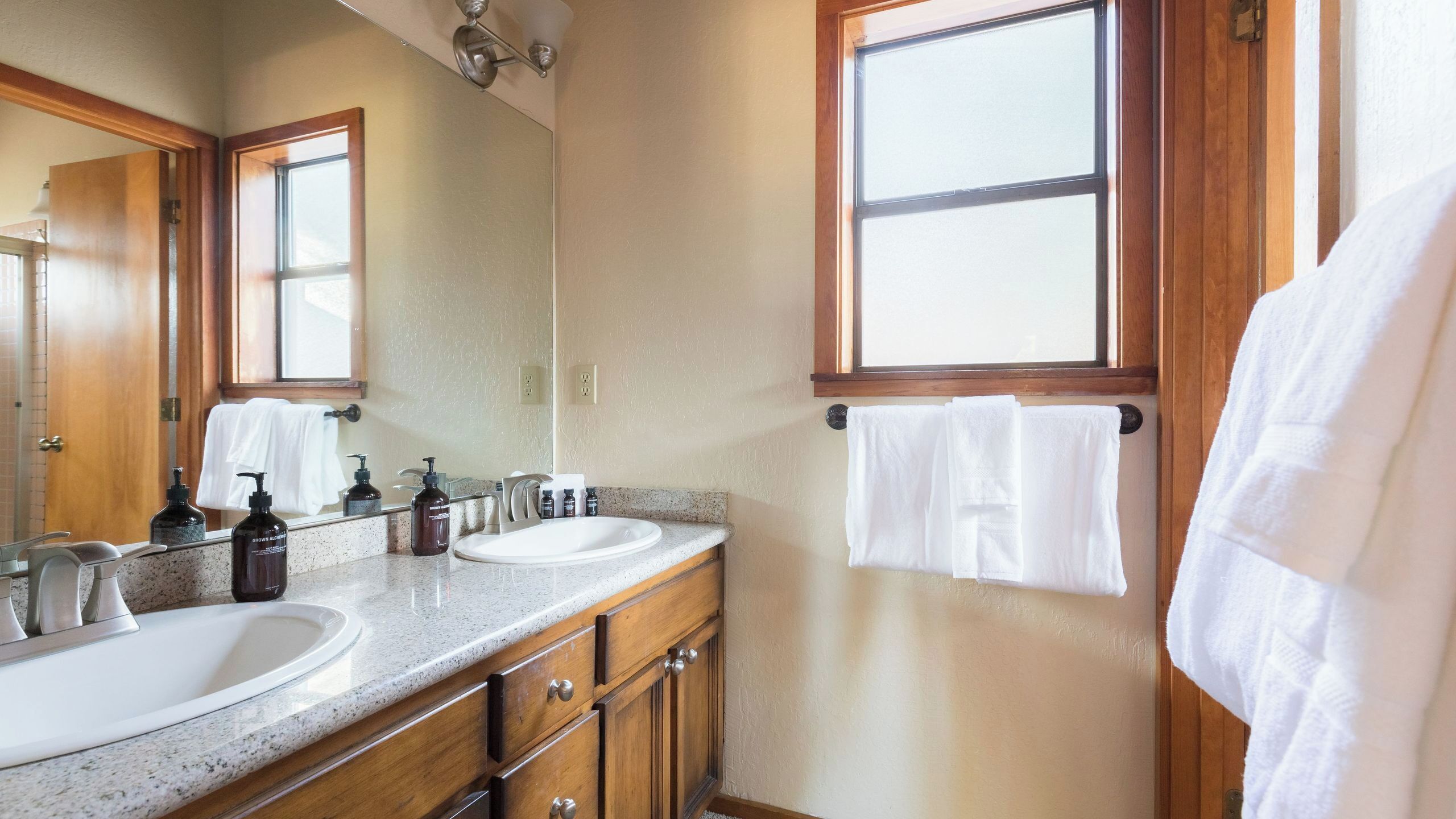 A bathroom with two sinks, wooden cabinets, a large mirror, and towels hanging on the wall.
