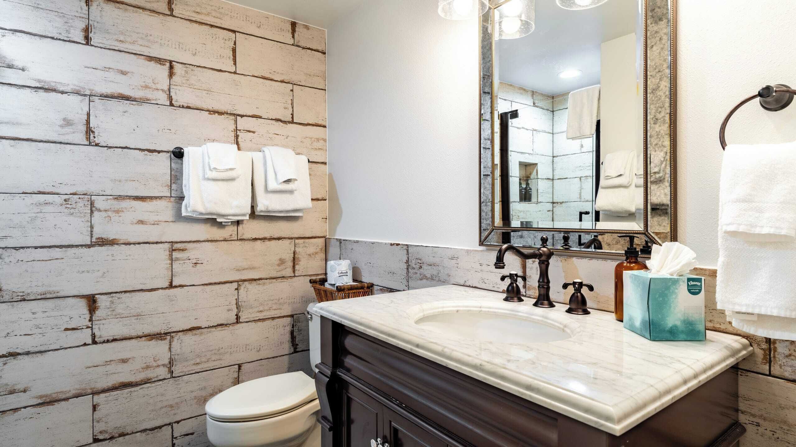 A bathroom with a rustic brick wall, a marble sink, a large mirror, and a toilet.