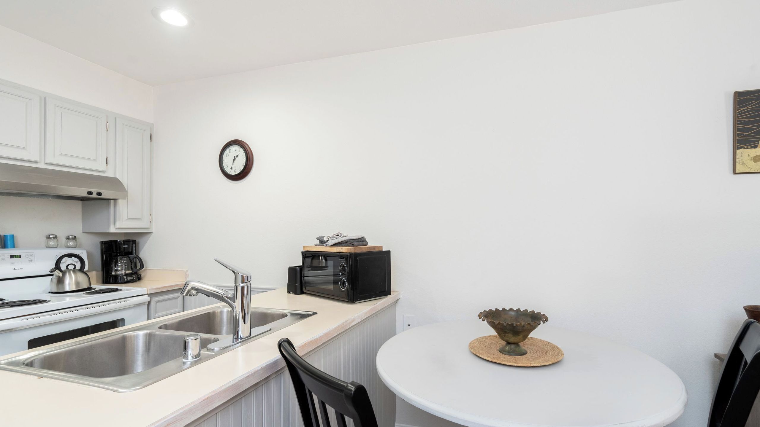 Een keuken met een fornuis, spoelbak, magnetron en een klok aan de muur.
