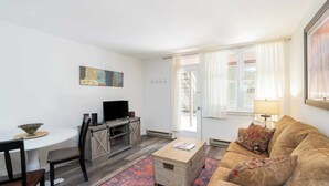 Een woonkamer met een televisie, een houten salontafel, een bank, een eettafel met stoelen en een vloerkleed.