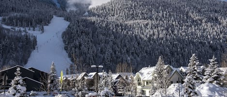A snow-covered mountain with a ski slope, houses with snow-covered roofs, and a clear sky.