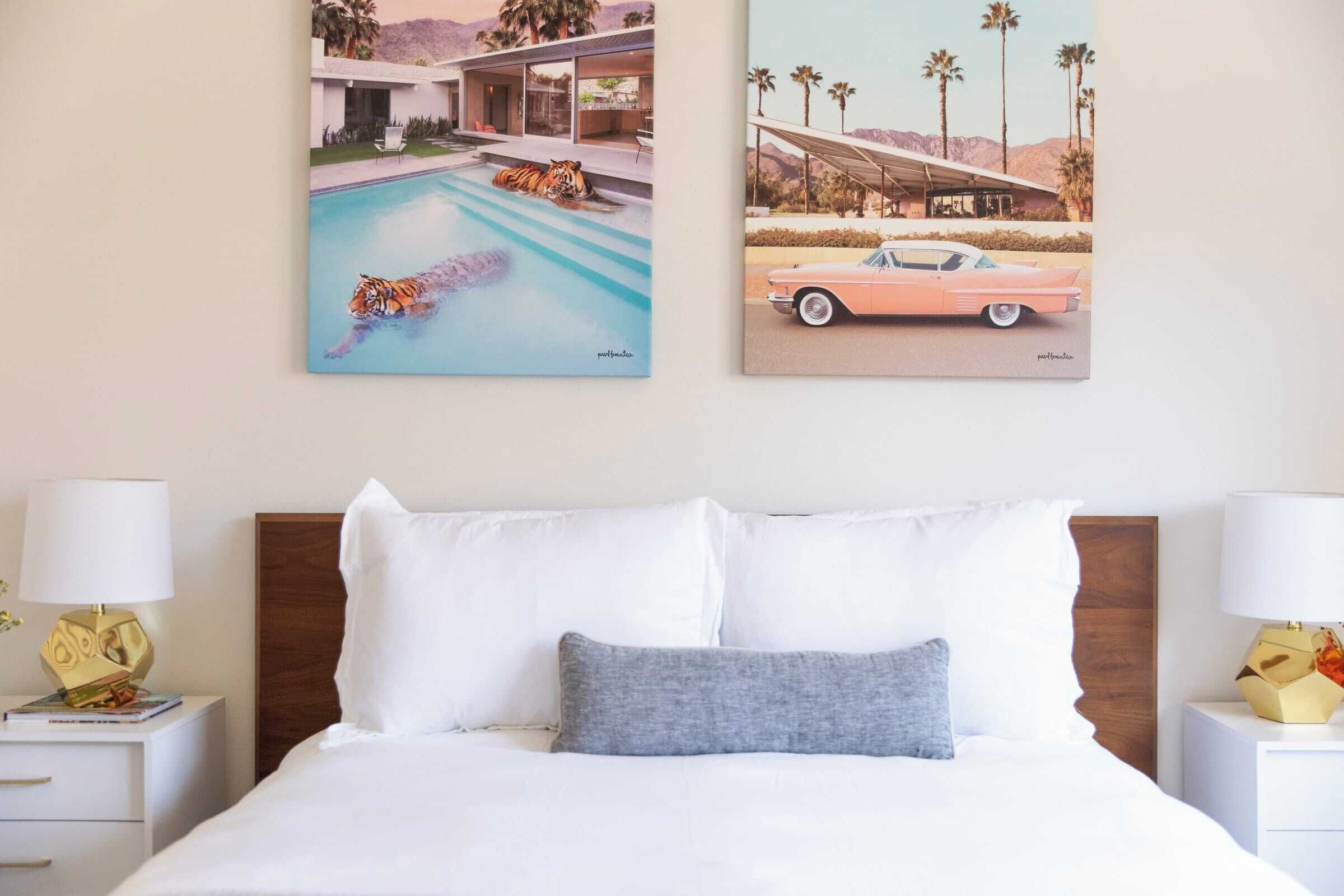 Une chambre à coucher avec un lit, deux tables de chevet et deux lampes. Deux tableaux sont accrochés au mur, l’un représente un tigre dans une piscine et l’autre, une voiture rose.