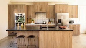 A modern kitchen with wooden cabinets, stainless steel appliances, and a central island with stools. - Marilyn by Avantstay Mins to Old Town La Quinta! (La Quinta)
