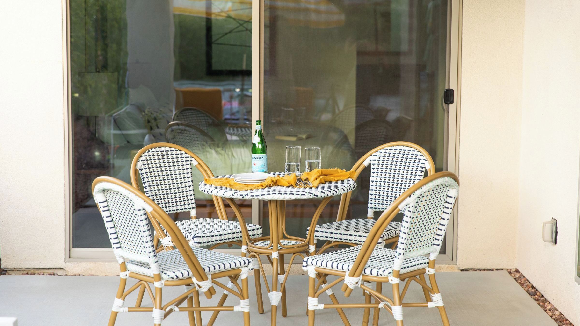 Un ensemble de chaises en osier et une petite table sur laquelle se trouvent une bouteille et des verres, le tout placé sur une terrasse.