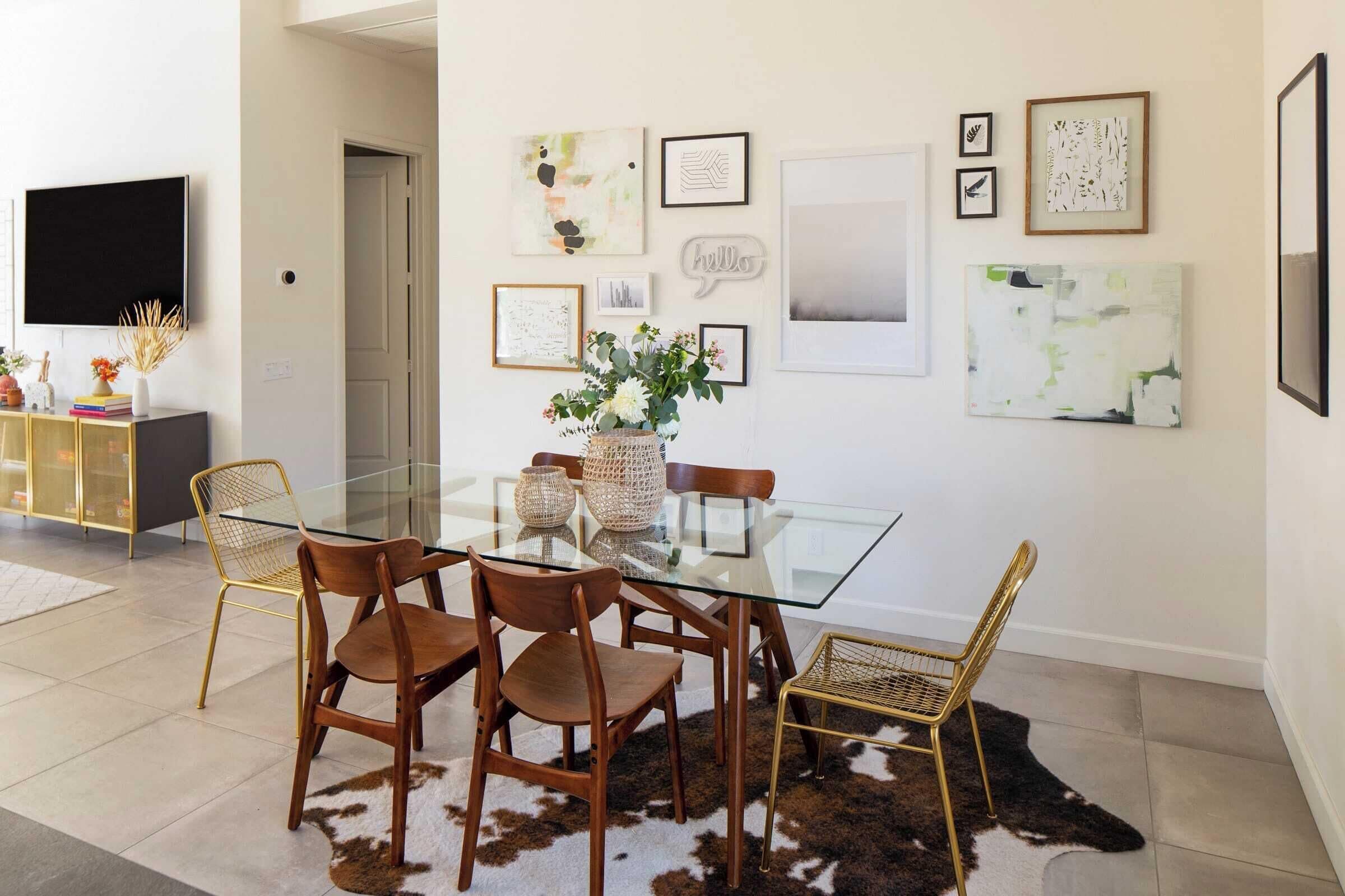 A dining area with a glass table, wooden chairs, and a cowhide rug.