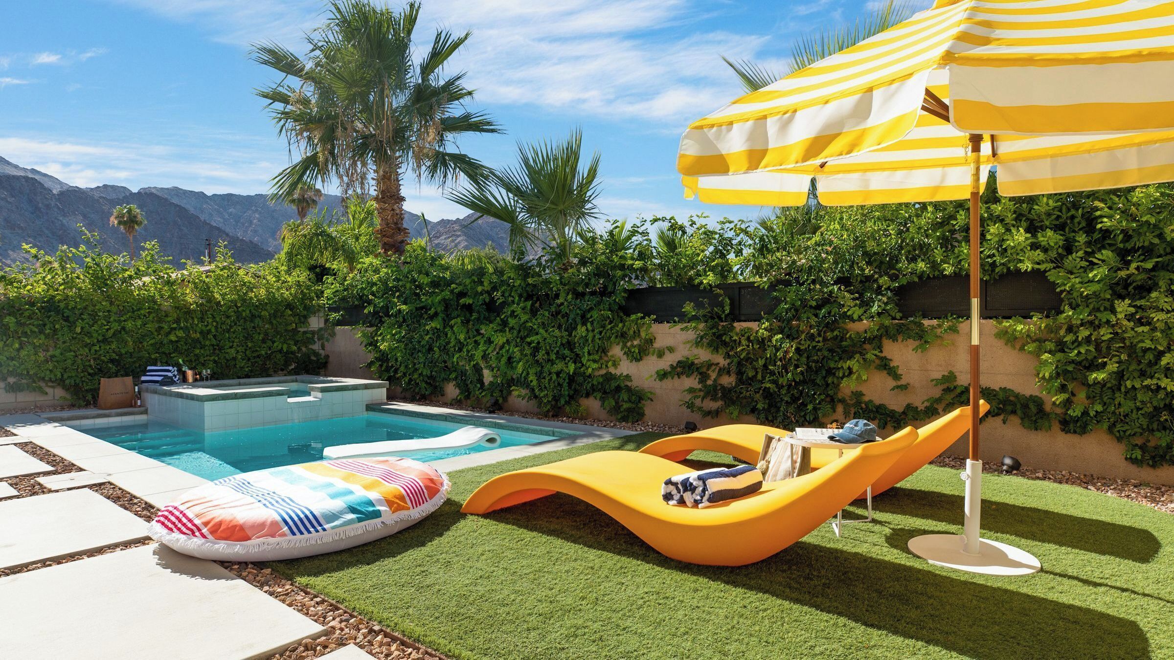 Una piscina con hidromasaje, tobogán y una silla de descanso amarilla con sombrilla.