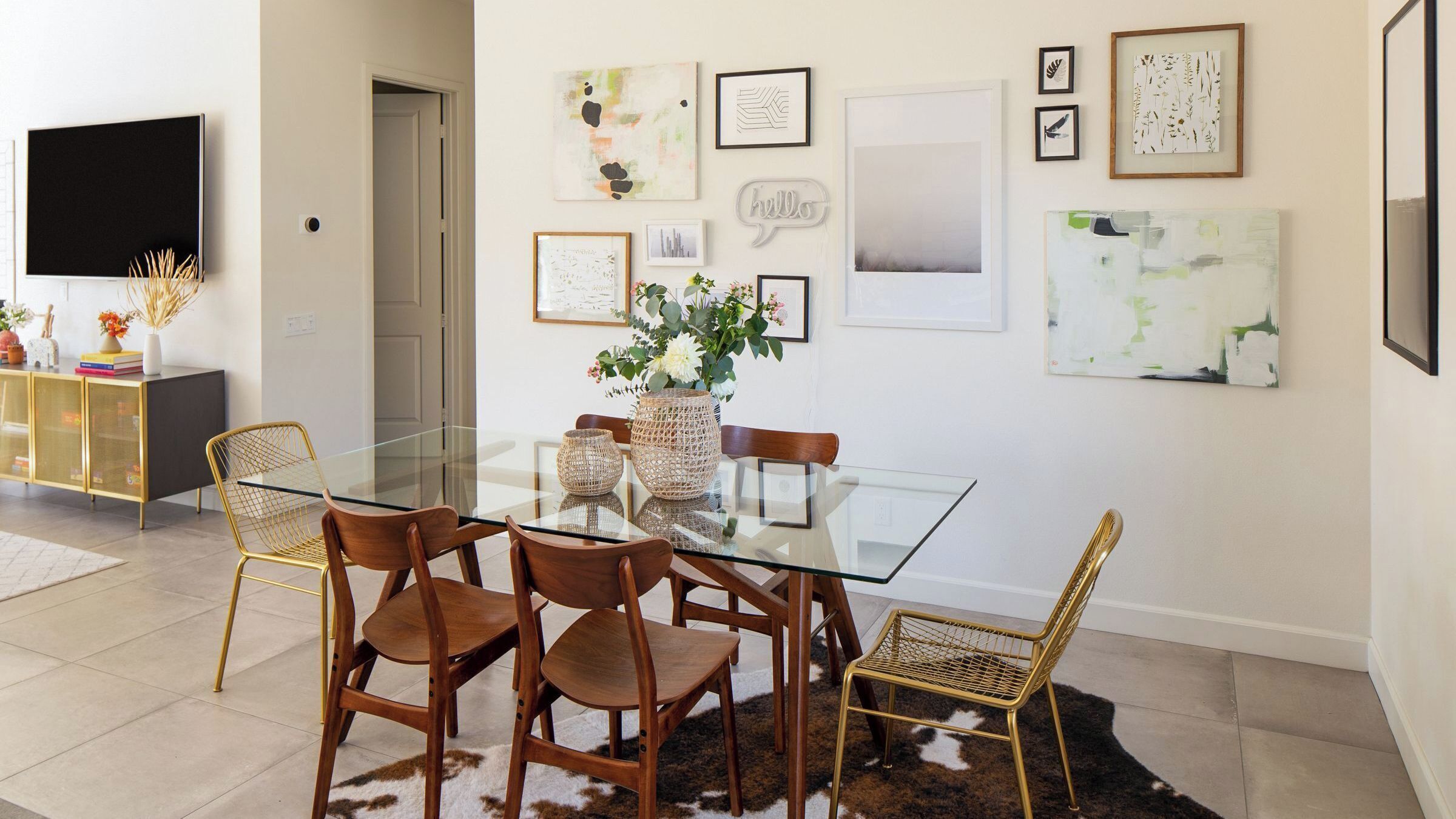 A dining area with a glass table, four chairs, and a vase of flowers.